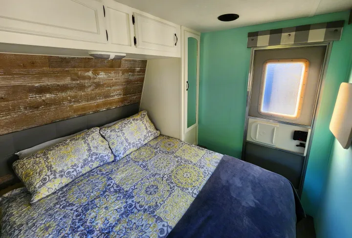 Bright rv rental bedroom with a cozy patterned bed, rustic wood accent wall, white cabinets, and serene teal walls.. Forest River Palomino Puma 2009