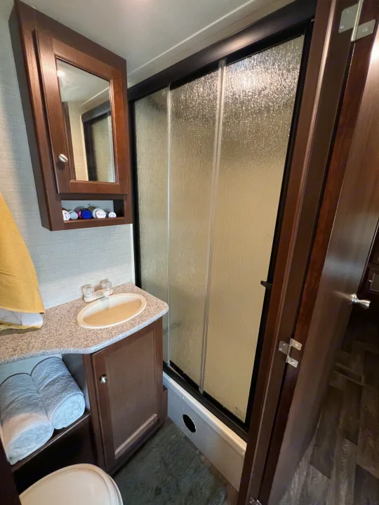 Inside an RV rental, a compact bathroom: sink, mirrored cabinet, and frosted glass shower visible. Rolled towels below.. Keystone RV Bullet Ultra Lite 2016