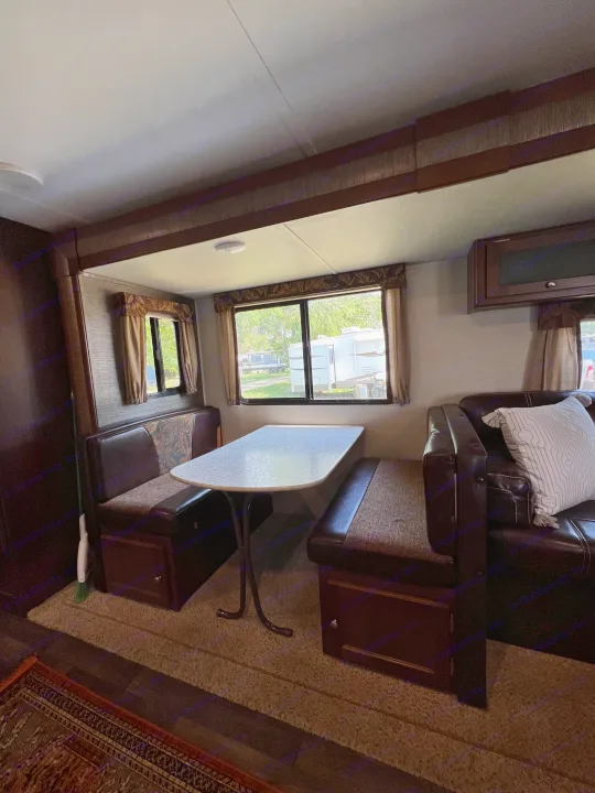 Cozy RV rental interior: Dinette with table & benches, sofa lounge area. Bright windows show other RVs outside.. Keystone RV Bullet Ultra Lite 2016