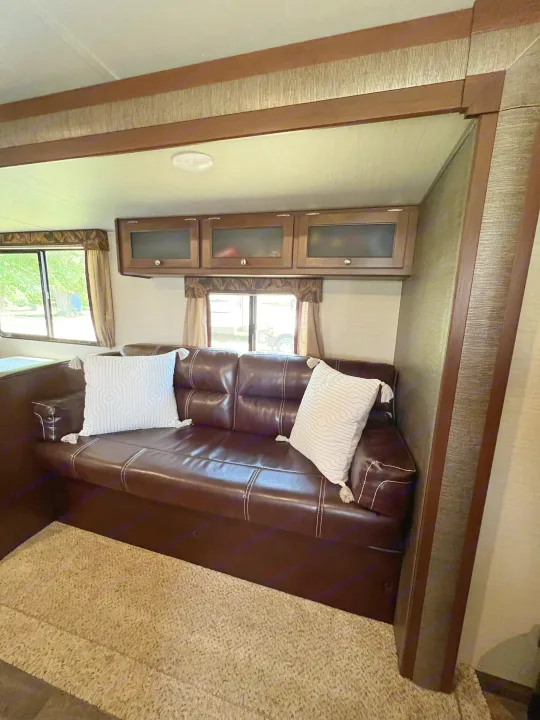 Spacious RV rental interior featuring a comfy brown sofa, overhead cabinets, and large windows, ready for adventure.. Keystone RV Bullet Ultra Lite 2016