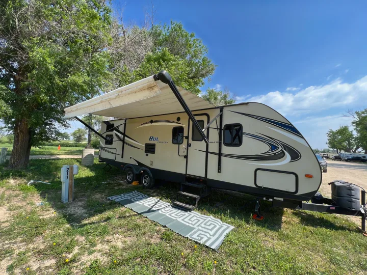 Spacious rv rental travel trailer with an extended awning set up at a sunny campsite (site 217) for comfortable outdoor living.. Keystone RV Bullet Ultra Lite 2016
