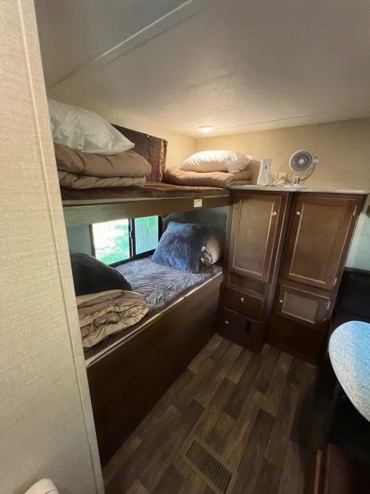 Inside an **RV rental**: a cozy sleeping area with upper and lower **bunk beds**, a bedside fan, and storage cabinets.. Keystone RV Bullet Ultra Lite 2016