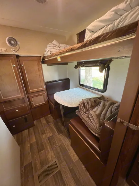 Inside a cozy RV rental: bunk beds, dining table, built-in storage, and a window view. Ideal for trips.. Keystone RV Bullet Ultra Lite 2016