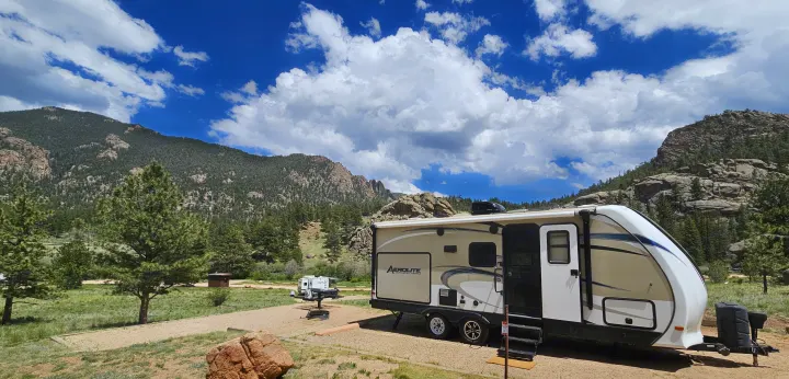 RV rental at a scenic mountain campsite, surrounded by pine trees under a vibrant blue sky with fluffy clouds. Ideal for camping.. Dutchmen Aerolite 2017