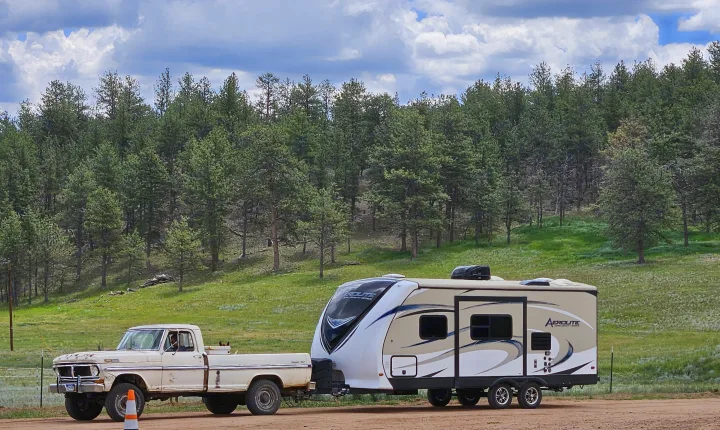 A classic truck with a dog tows an Aerolite RV rental in a forested setting, perfect for outdoor camping adventures.. Dutchmen Aerolite 2017