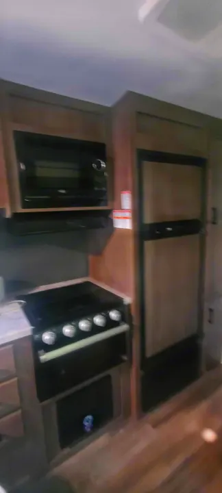 RV rental kitchen: microwave, gas range, oven, and two-door refrigerator are clearly seen within wood-toned cabinetry.. Starcraft Autumn Ridge 2022
