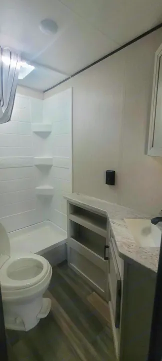 Modern and clean RV rental bathroom, featuring a white toilet, stand-up shower, and a vanity with stone-look countertop.. Starcraft Autumn Ridge 2022