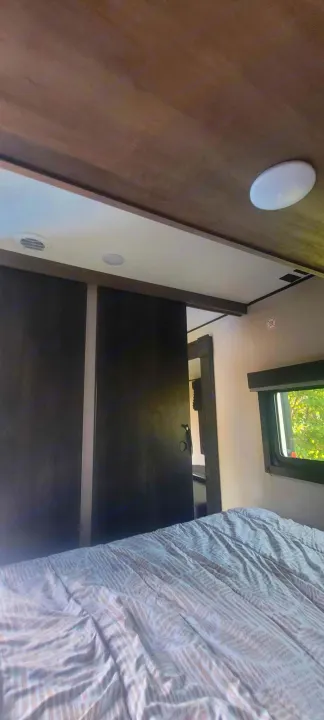 Cozy RV rental bedroom interior with patterned bedding, dark sliding doors, and a window showing greenery.. Starcraft Autumn Ridge 2022