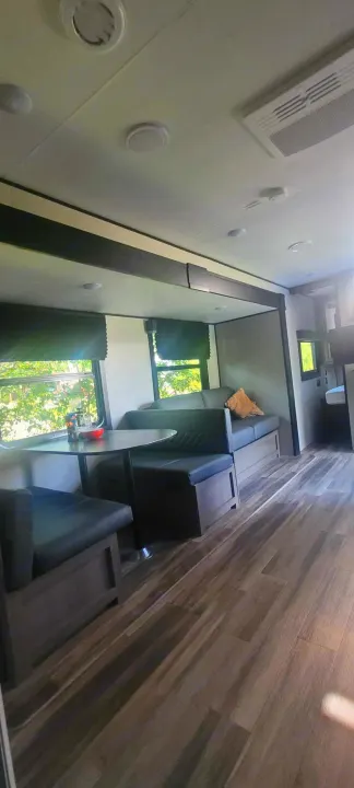 Inside a modern RV rental: A spacious living area with a dark cushioned dinette, wood flooring, and large windows.. Starcraft Autumn Ridge 2022