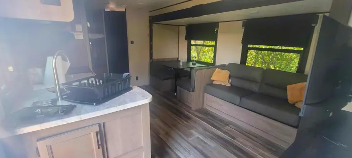 RV rental interior view: kitchen counter with sink, dining booth, and a cozy sofa next to sunlit windows.. Starcraft Autumn Ridge 2022