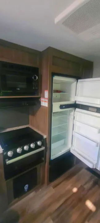 View of a clean RV rental kitchen, featuring a microwave, stove, and an empty, open refrigerator.. Starcraft Autumn Ridge 2022