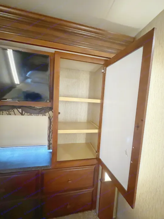 Inside an RV rental bedroom, showing an open wooden cabinet with empty shelves, a Sony TV, and lower drawers.. Newmar Canyon Star 2016