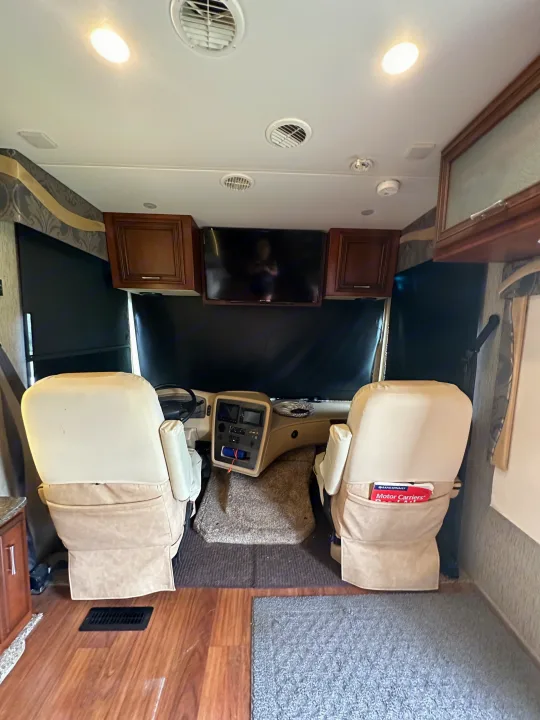 This RV rental's front cockpit features beige driver/passenger seats, dashboard controls, and an overhead TV, ready for your next journey.. Newmar Canyon Star 2016
