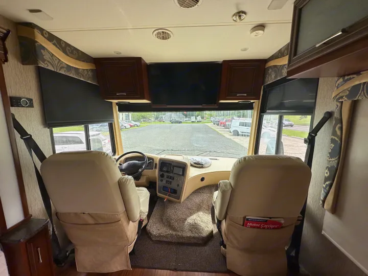 RV rental interior: driver's cockpit view with captain's chairs, dashboard, and overhead TV.. Newmar Canyon Star 2016