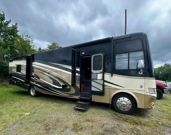 Sleek black & tan RV rental: a spacious motorhome with extended slide-outs and open steps, parked on gravel.. Newmar Canyon Star 2016