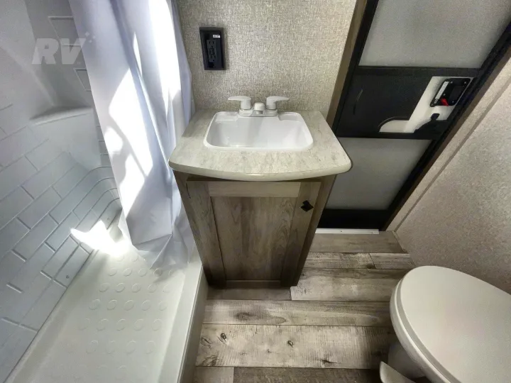 Compact RV rental bathroom with sink, shower, and toilet, featuring wood-look floor and textured walls.. KZ Sportsmen SE 2021