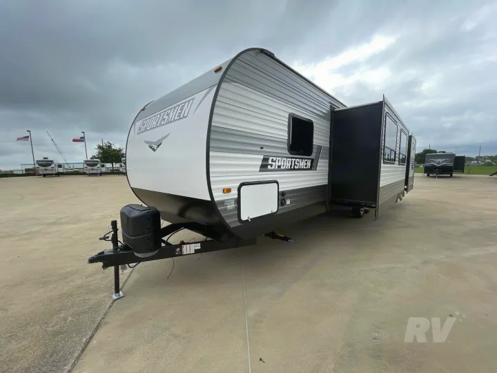 A gray & white Sportsmen travel trailer, ideal for rv rental, parked with its slide-out extended on a concrete lot.. KZ Sportsmen SE 2021