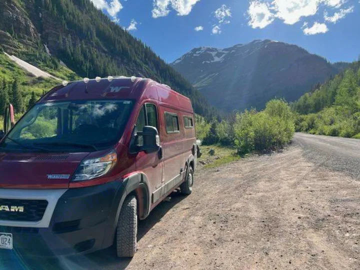 Red **RV rental** parked on a scenic mountain road. Enjoy majestic peaks and forests for your next adventure.. Winnebago Solis Pocket 2022