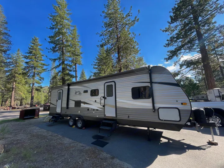 RV rental travel trailer, a Jay Flight model, set up at a scenic campsite with tall pine trees.. Jayco Jay Flight SLX 2021
