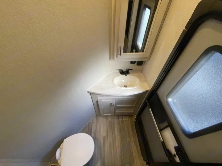 Inside an RV rental: a compact bathroom with toilet, corner vanity, sink, and mirror, perfect for on-the-go living.. Keystone Sprinter 2022