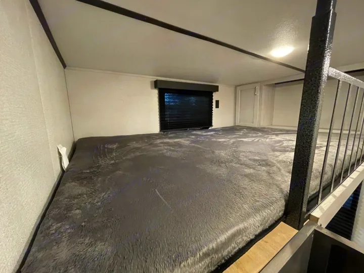 Cozy loft bed in an RV rental, featuring a plush grey blanket and safety railing, perfect for comfortable sleeping.. Keystone Sprinter 2022