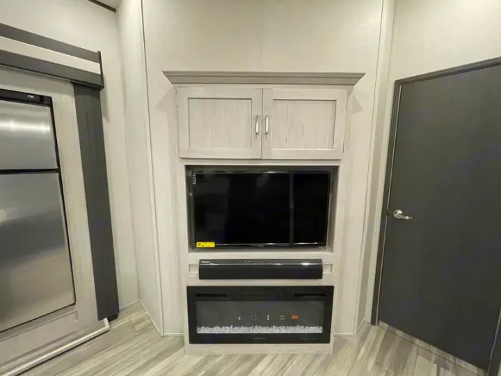 RV rental interior: Light-toned entertainment center with TV, soundbar, and electric fireplace. Fridge and door visible.. Keystone Sprinter 2022