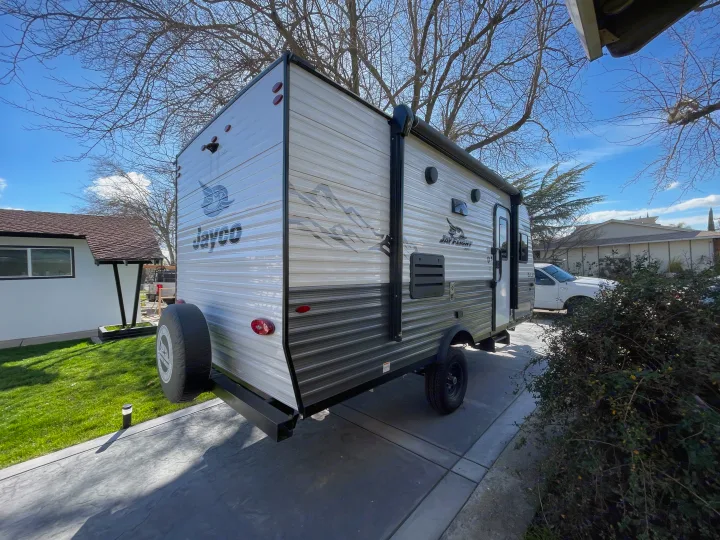 Detailed view of a white and gray Jayco travel trailer RV rental, parked on a sunny residential driveway.. Jayco Jay Flight SLX 2022