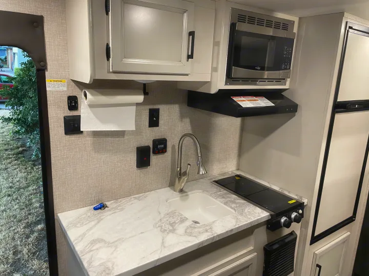 Functional RV rental kitchen with a sink, two-burner stovetop, microwave, and refrigerator for road trips.. Jayco Jay Flight SLX 2022