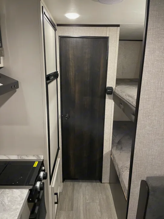RV rental showcasing a compact kitchen with stove & fridge, a central door, and bunk beds for family comfort.. Jayco Jay Flight SLX 2022