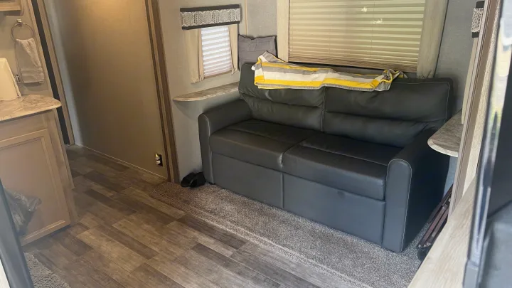 Inside an RV rental: a comfy dark sofa with striped blanket, window, and wood-look floor.. Coachmen Catalina 2021