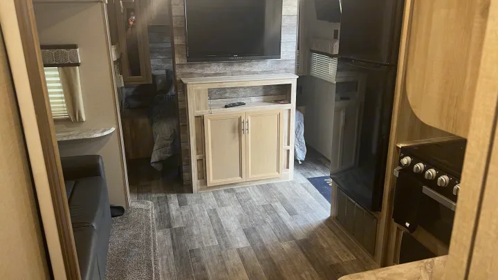 Step inside this RV rental: a modern living space with a large TV, comfortable sofa, and a compact kitchen area with a fridge and stove.. Coachmen Catalina 2021