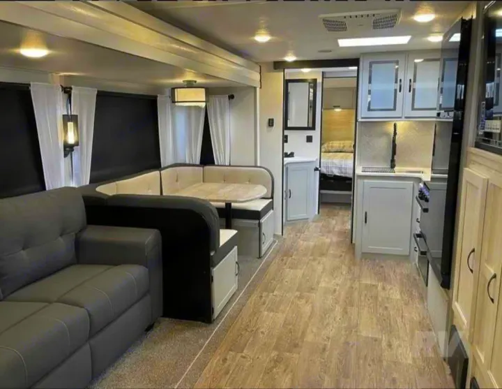 RV rental interior showcasing a modern kitchen, U-shaped dining booth, gray sofa, and bedroom access. Bright and comfortable living space.. Forest River Vibe 2022