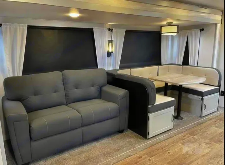 This RV rental's modern interior features a gray sofa, a U-shaped dinette with light table, and black window shades.. Forest River Vibe 2022