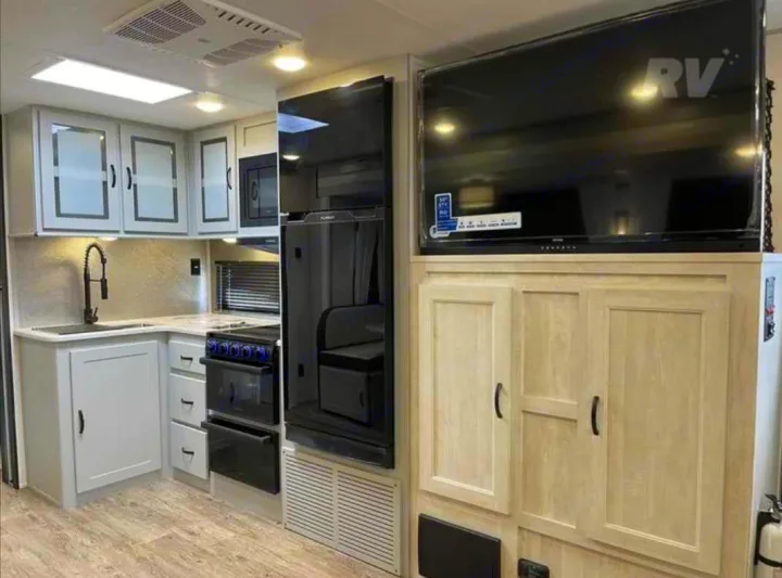 Modern RV rental interior featuring a complete kitchen with appliances and a large TV entertainment area.. Forest River Vibe 2022