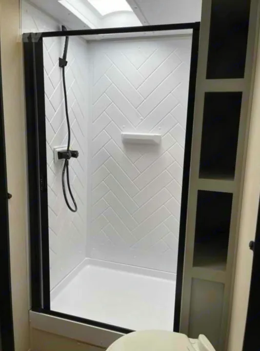 Modern shower in an RV rental, featuring white herringbone walls, black fixtures, and a glass door. Bright, clean RV bathroom interior.. Forest River Vibe 2022