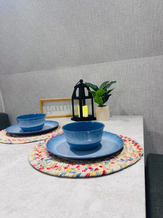 Cozy dining setup in an RV rental, featuring blue dishes, colorful placemats, and decorative accents for a welcoming meal.. Braxton Creek Bushwhacker Plus 2021