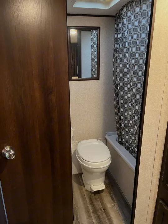 Compact RV rental bathroom featuring a white toilet, shower with geometric curtain, and wall mirror.. Jayco Jay Flight SLX 2020