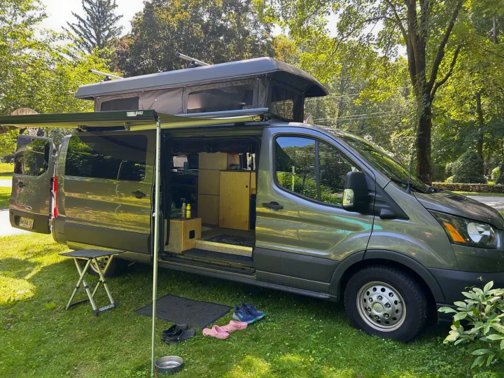 This RV rental camper van with a pop-top roof and extended awning offers a comfortable outdoor setup for adventure travel.. Ford Custom Transit 2022