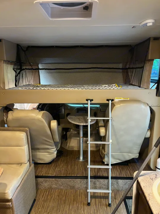 Spacious RV rental interior featuring an overhead bunk bed, ladder, and front cabin area. Ideal for camper adventures.. Thor Axis 2017
