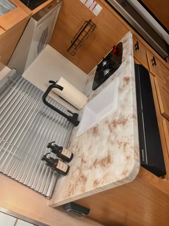 This RV rental features a compact kitchen with a stovetop, covered sink, paper towels, and a Furrion soundbar.. Avenger LT 2022