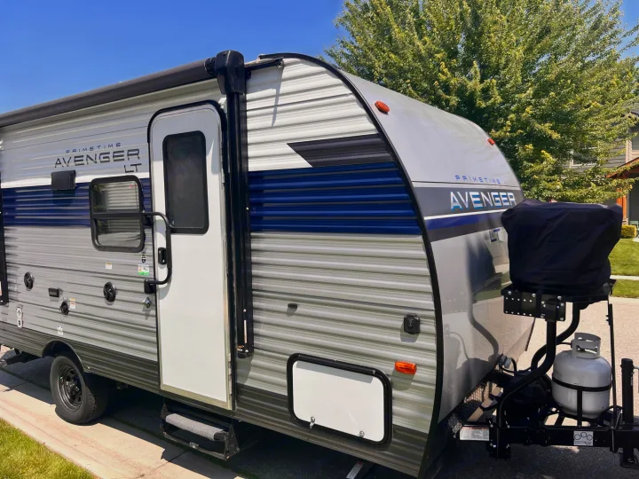 View of a gray Primetime Avenger LT travel trailer RV, ideal for RV rental adventures. Features an awning & blue accents.. Avenger LT 2022