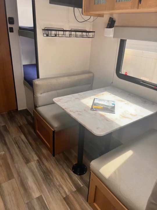 An RV rental's inviting dinette area with seating, table, and storage, bathed in natural light from the window.. Avenger LT 2022