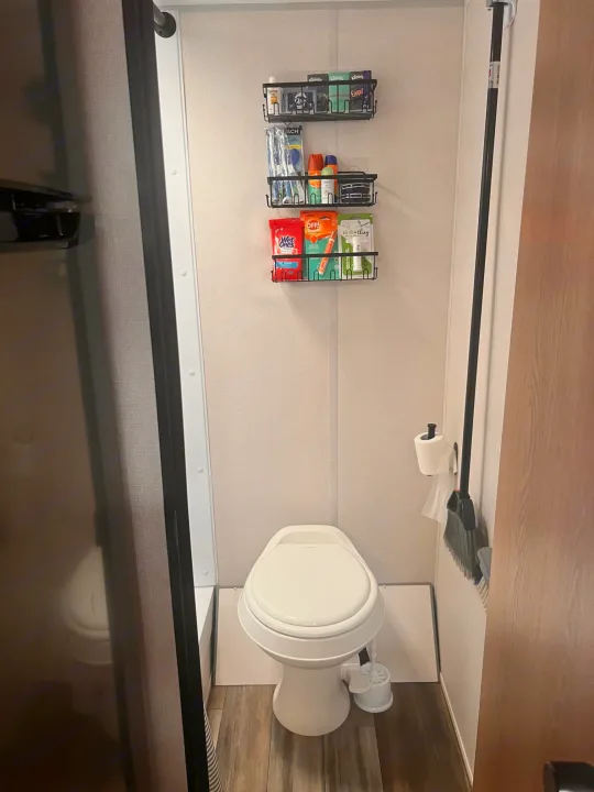 Compact RV rental bathroom: toilet, wall-mounted broom, and organized storage for everyday essentials.. Avenger LT 2022