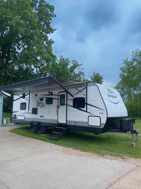 A white Jayco Jay Flight SLX travel trailer RV rental with an extended awning, parked on grass next to a concrete pad.. Jayco Jay Flight SLX 2017