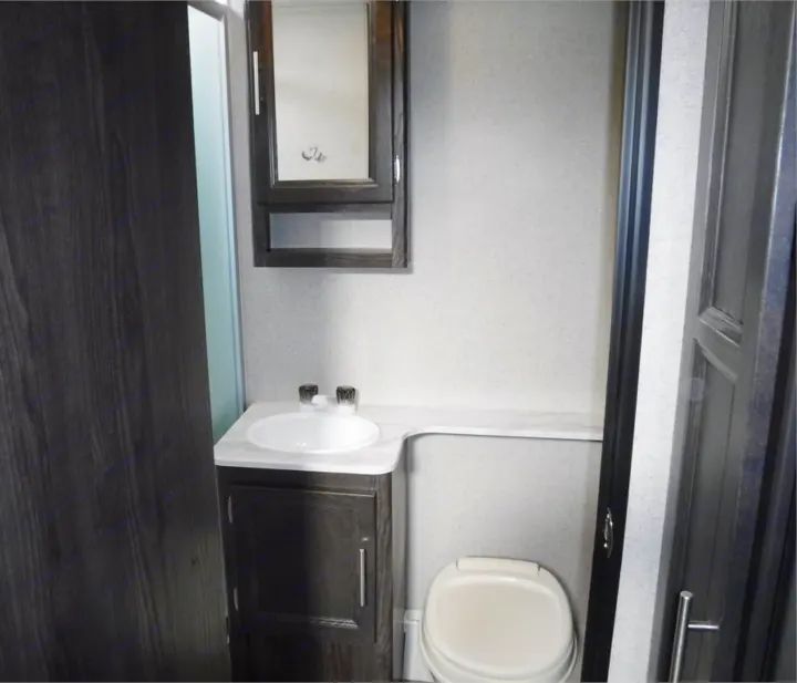 Compact RV rental bathroom features a white sink, toilet, and dark wood medicine cabinet. Ideal for travel.. Dutchmen Kodiak Ultimate 2018
