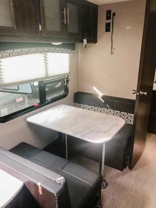 Inside an RV rental: a modern dinette with a light-colored table, black benches, window, and entertainment wall.. Dutchmen Kodiak Ultimate 2018