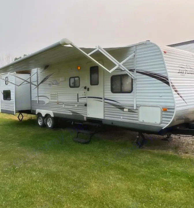 White travel trailer rv rental with extended awning & slide-out, parked on green grass. Ready for adventure.. Jayco Jay Flight 2012