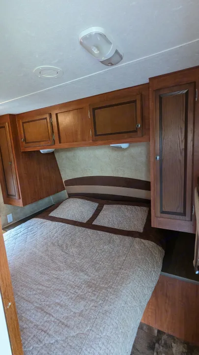 Cozy RV rental bedroom with ample overhead storage, a comfortable bed, and wooden cabinets.. Jayco Jay Flight 2012