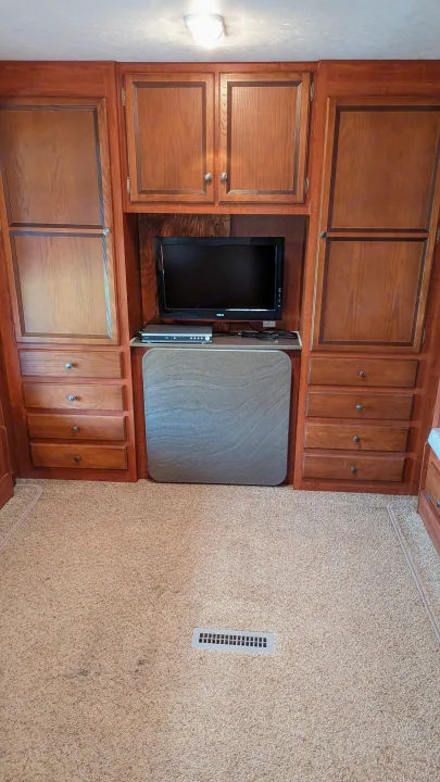 Cozy RV rental interior with rich wooden cabinetry, built-in TV, DVD player, and storage. Beige carpeted floor & ceiling light.. Jayco Jay Flight 2012