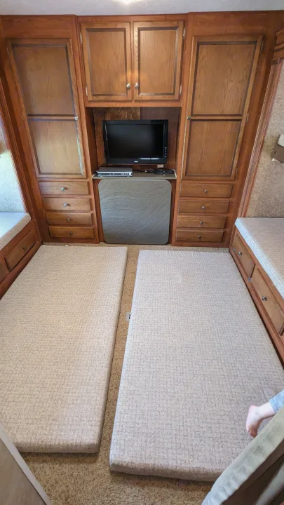 RV rental interior: two sleeping pads on carpeted floor, integrated wooden cabinetry with TV, and storage drawers.. Jayco Jay Flight 2012